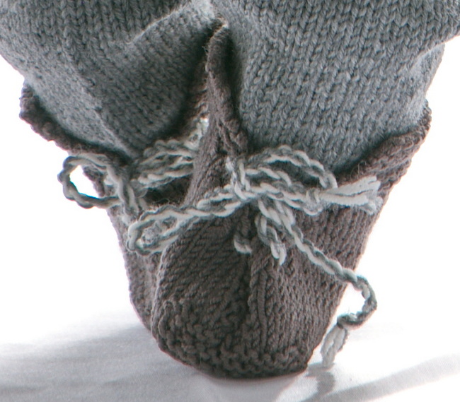 Skoene er strikket i brunt og knyttet foran med snorer tvunnet i grått og hvitt.