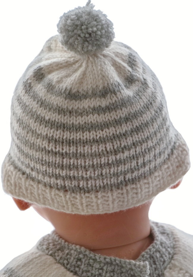 Le bonnet de la petite sœur est tricoté en rayures et à un pompon gris sur le dessus