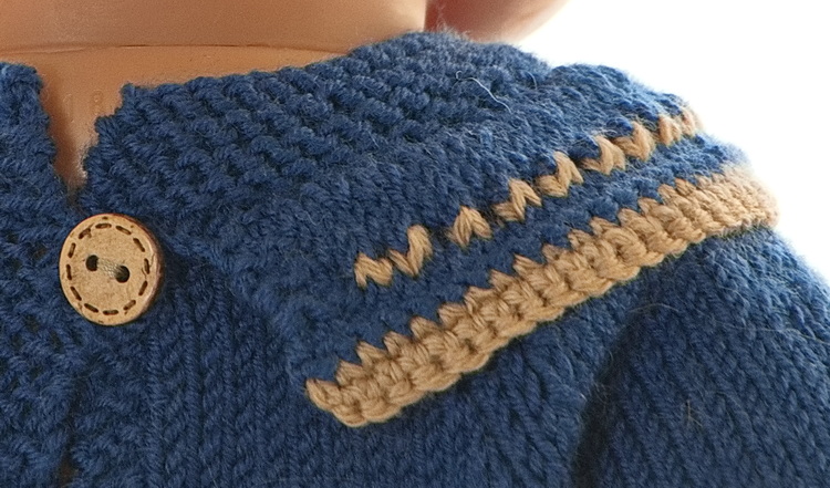 Le col est tricot en bleu avec un bord marron. Les bordures du costume et de la poche sont crochetées en marron. Le petit motif est une rangée d'oeillets tricotés en beige.