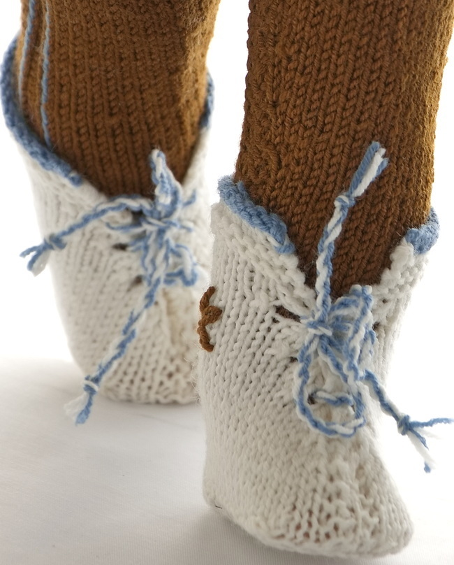 Superfine shoes are white with an edge around the ankles knitted in blue. A cord is made with one thread blue and one thread white thread and pulled through the eyelets knitted along each side of the opening front. A brown flower is sewn in loop stitches on the outside of the shoes.