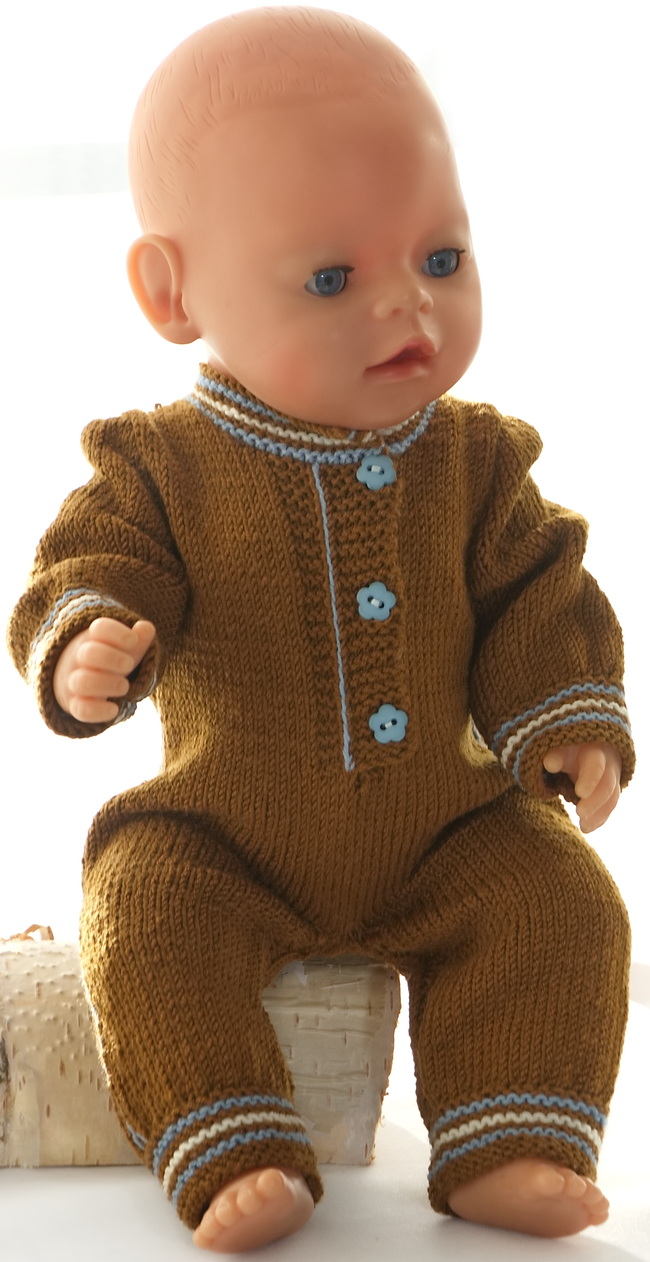 Baby born a une combinaison marron qui s'accorde très bien avec les vêtements de Dina. Elle est tricotée en marron et a les mêmes rayures que celles tricotées pour le pantalon de Dina sur les côtés. Elle est boutonnée à l'avant. Le bord le long de l'ouverture à l'avant est tricoté en point mousse avec une ligne en points arrière bleus cousus entre les mailles au point mousse. Cette bande bleue est utilisée à plusieurs endroits entre la couleur marron et rend les vêtements spéciaux. De petits boutons bleus cousus le long de l'ouverture à l'avant rendent la combinaison remarquable.