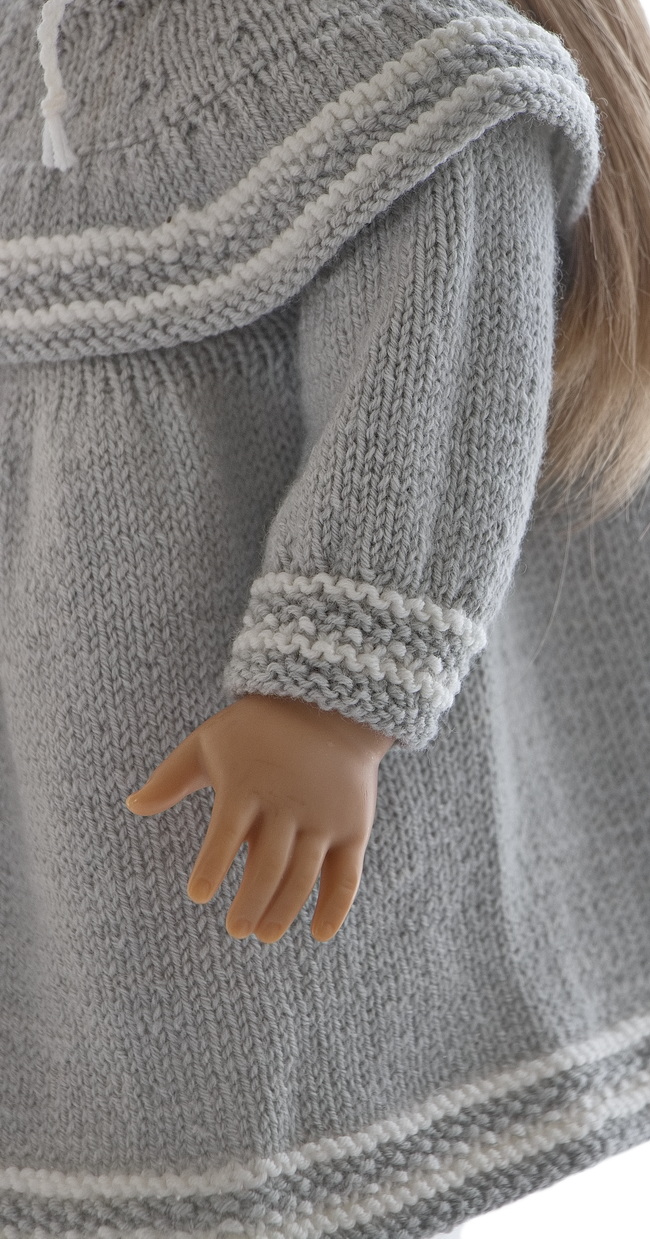 Die Handgelenke an den Ärmeln haben das gleiche schöne Muster wie am Saum. Ein einfacher Kragen, gestrickt im Perlmuster, hat einen kleinen weißen Rand oben herum. Um die Schultern herum hat das Kleid eine großartige und schöne Rüsche, gestrickt in grau mit dem gleichen Rand wie an den anderen Rändern. Ein einzigartiges und wunderschönes Kleid für jede Feier und zum Spielen mit Ihren lieben Puppen.