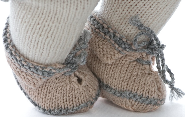 The shoes are knitted in beige and grey. They are folded around the legs and bound in a grey bow front