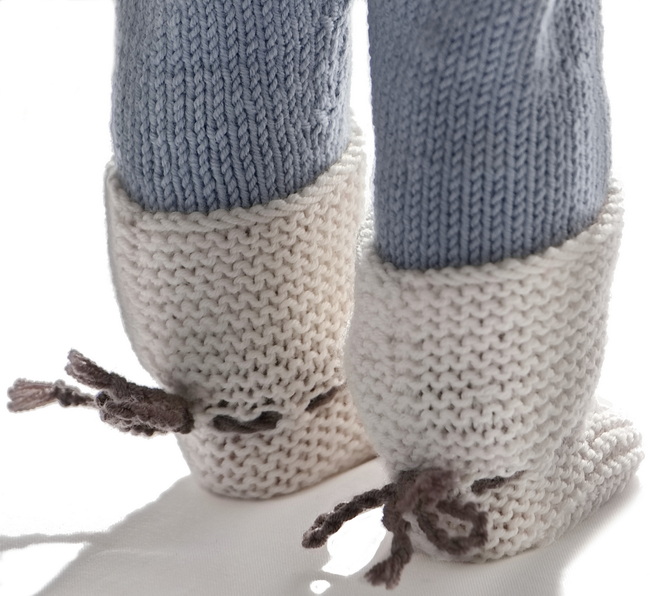 Socks/shoes knitted in garter sts. Along the front, the shoes/socks have the same fine cable. They are bound around the ankles with a brown cord.